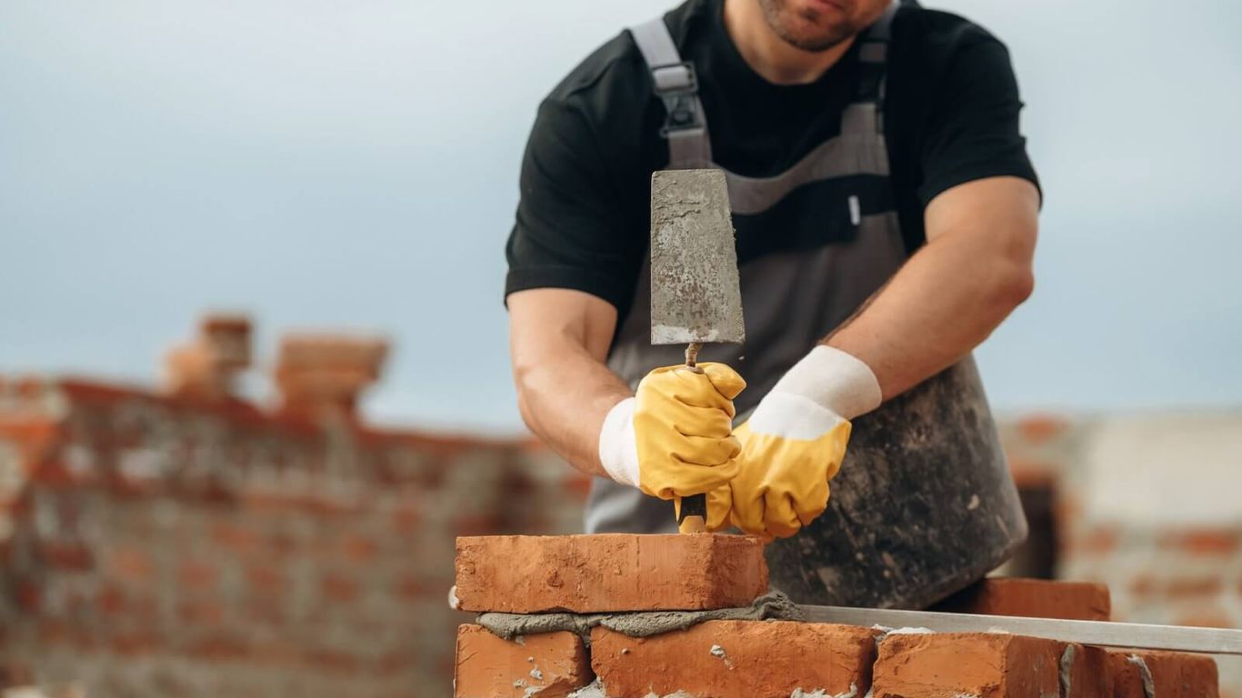 A person is building a brick wall with a trowel and mortar.