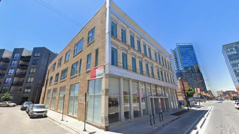 Corner building with brick facade and modern additions on a sunny day.