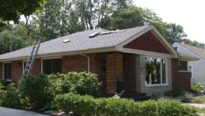 A ladder leans against a brick house with roof repairs underway.