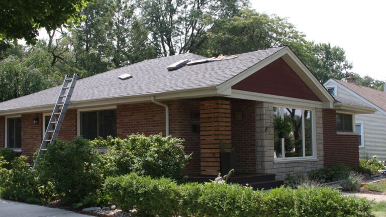 A ladder leans against a brick house with roof repairs underway.