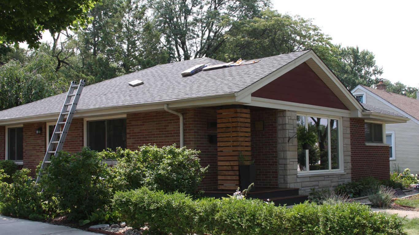 A ladder leans against a brick house with roof repairs underway.