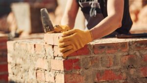 A person wearing gloves places a brick on a wall.
