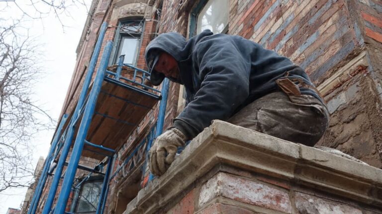 A person works on a brick building with scaffolding.