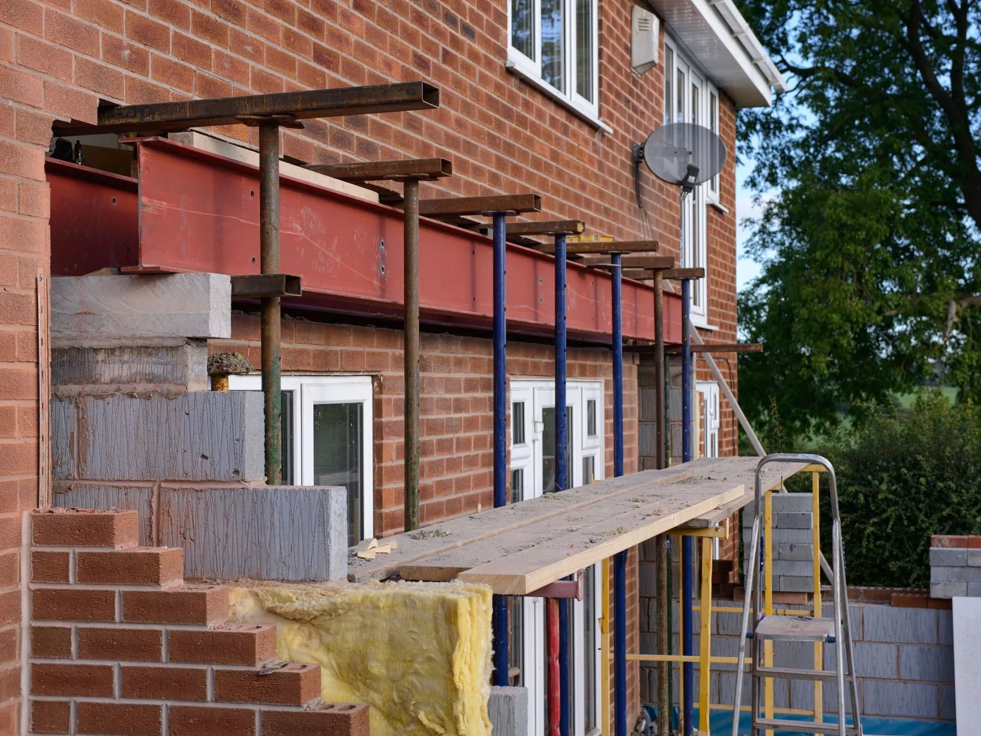 Construction site with scaffolding and steel beams supporting a brick wall.