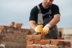 A professional mason using a trowel to apply mortar between bricks on a residential building.